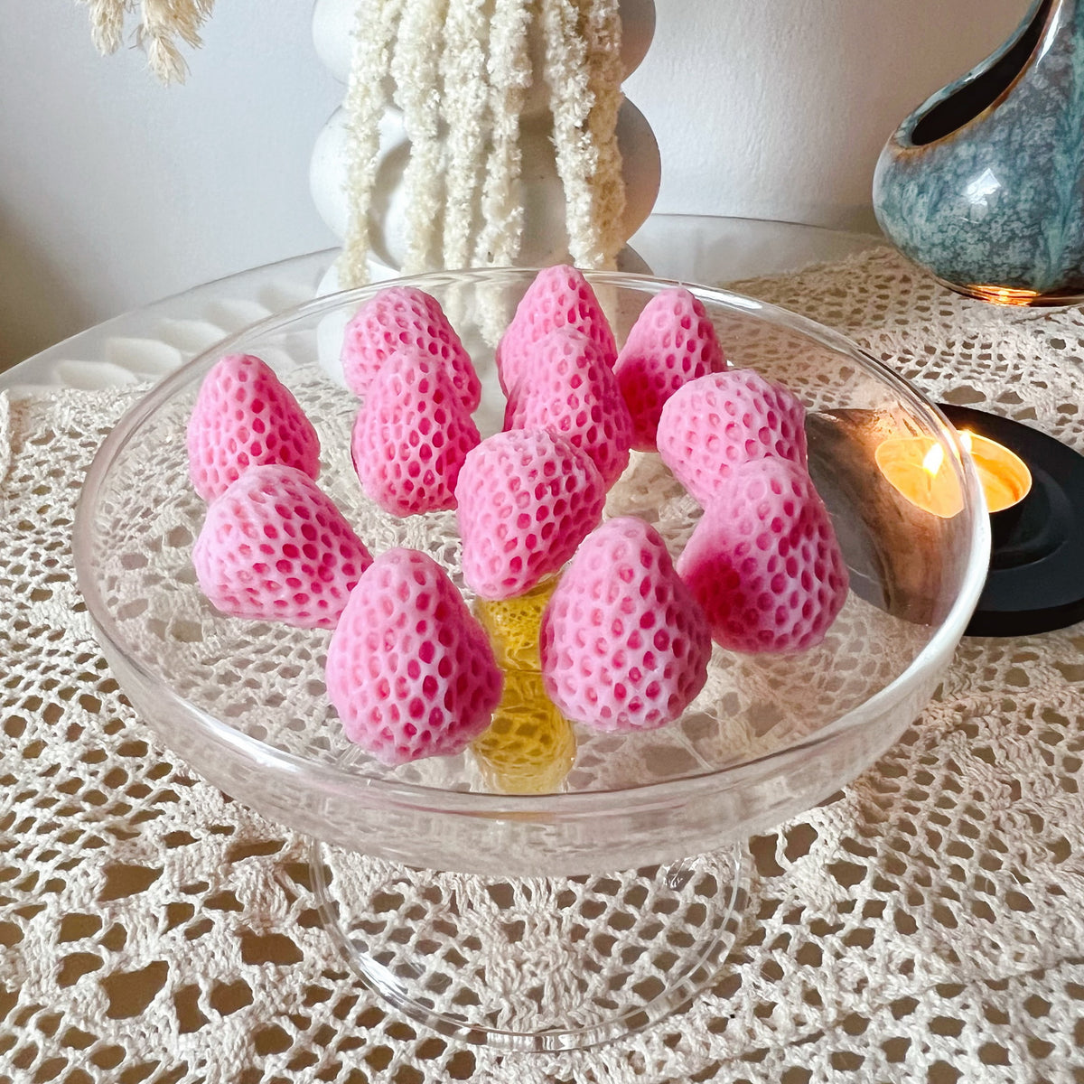 Pack of 12 vibrant red strawberry-shaped soy wax melts by LMJ Candles displayed on ceramic wax warmer and glazed tray, highlighting their unique fruit design and bright colour.