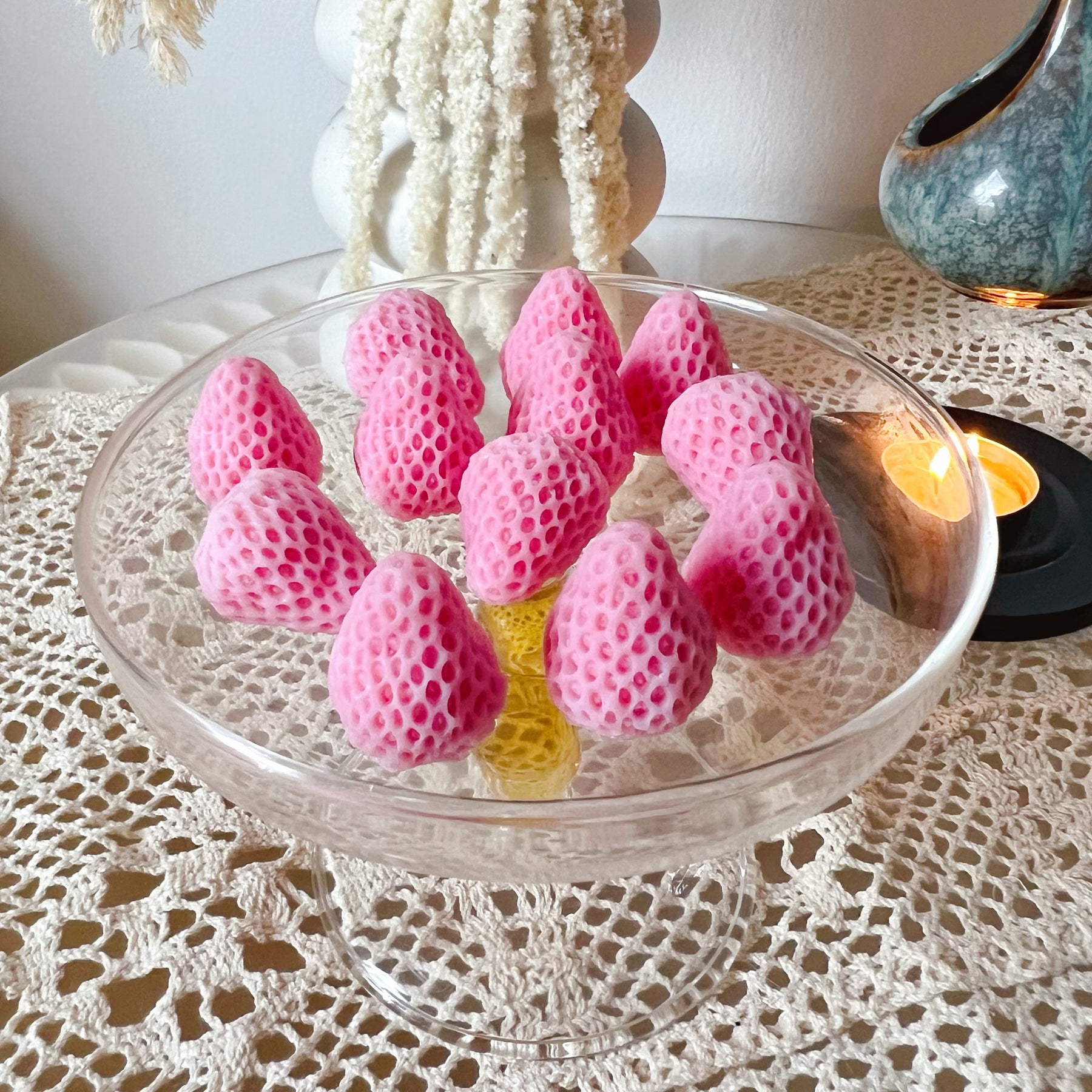 Pack of 12 vibrant red strawberry-shaped soy wax melts by LMJ Candles displayed on ceramic wax warmer and glazed tray, highlighting their unique fruit design and bright colour.