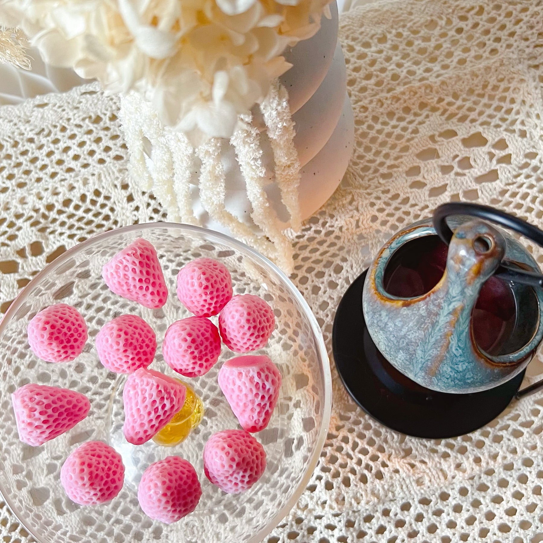 Pack of 12 vibrant red strawberry-shaped soy wax melts by LMJ Candles displayed on ceramic wax warmer and glazed tray, highlighting their unique fruit design and bright colour.