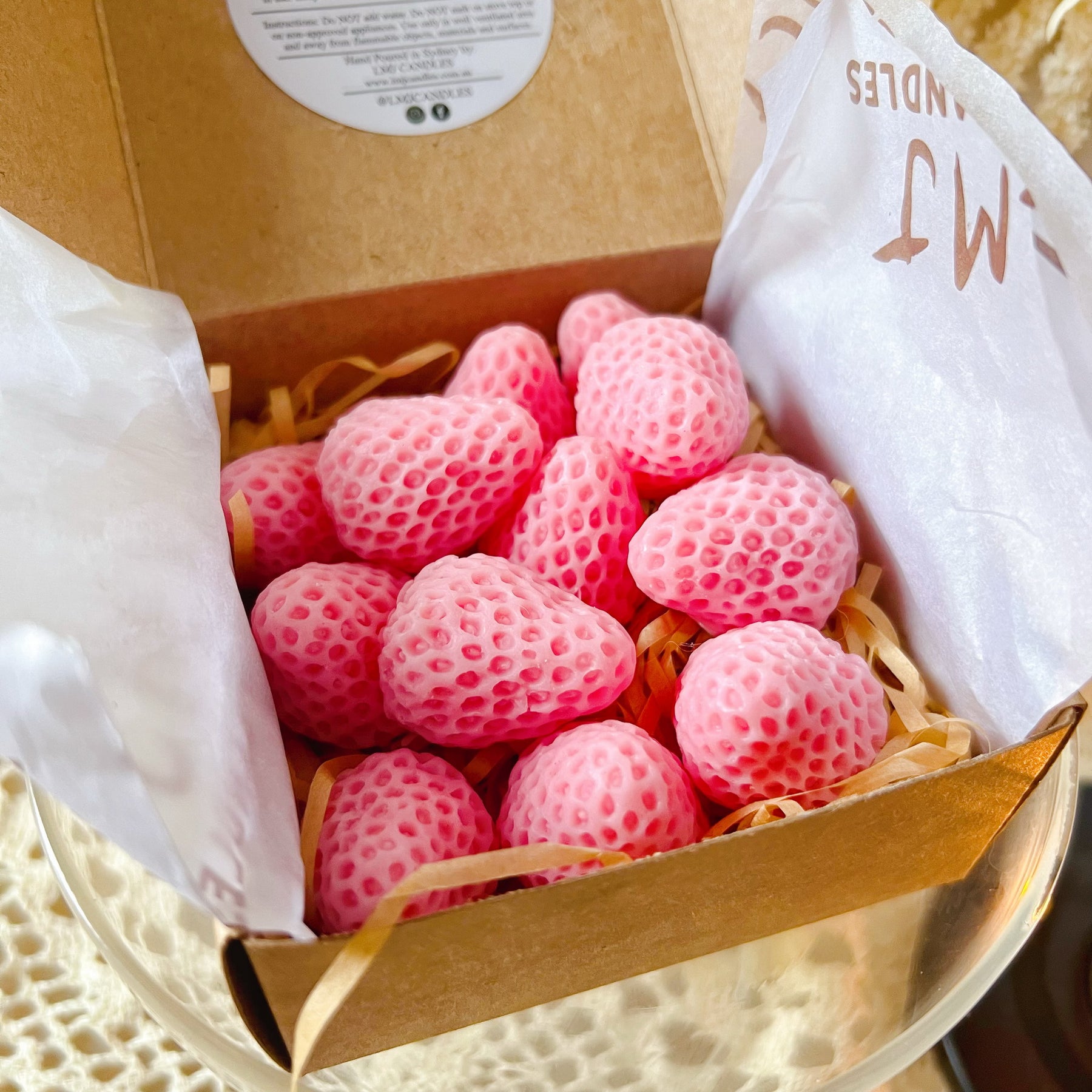 Pack of 12 vibrant red strawberry-shaped soy wax melts by LMJ Candles displayed on ceramic wax warmer and glazed tray, highlighting their unique fruit design and bright colour.